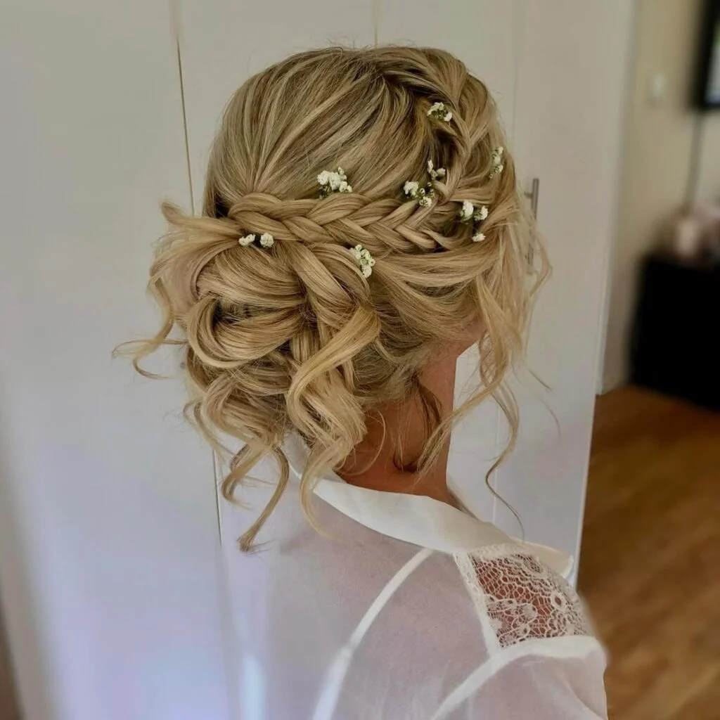 Low blonde braided bridal updo with baby’s breath flowers and loose curled tendrils.