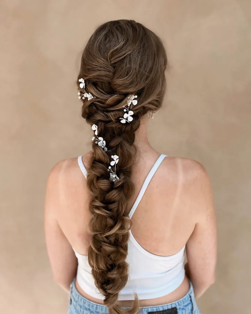Voluminous long brunette bridal braid with white leaf pins and textured woven sections.