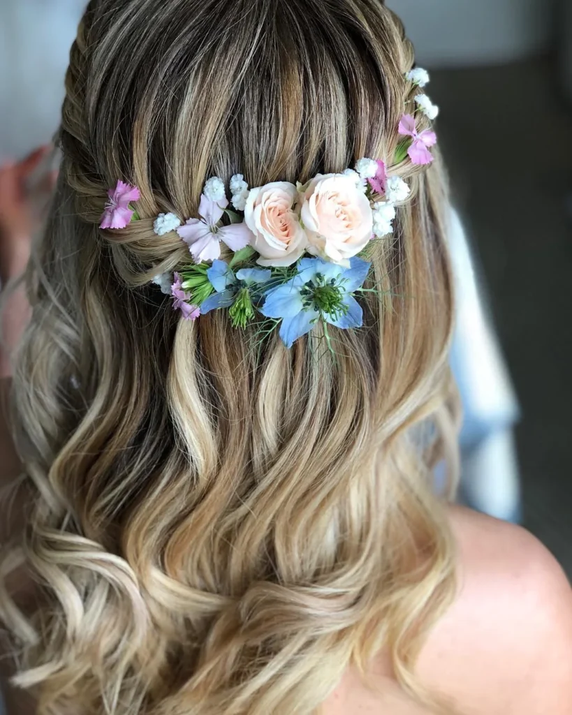 Blonde floral half-up bridal hairstyle with pink, blue and white flowers and loose waves.