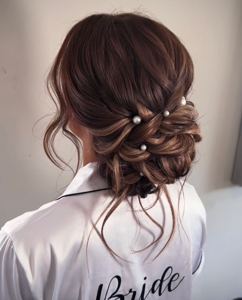 Textured brunette low bun with loose curls and scattered pearl hair pins for a bridal look