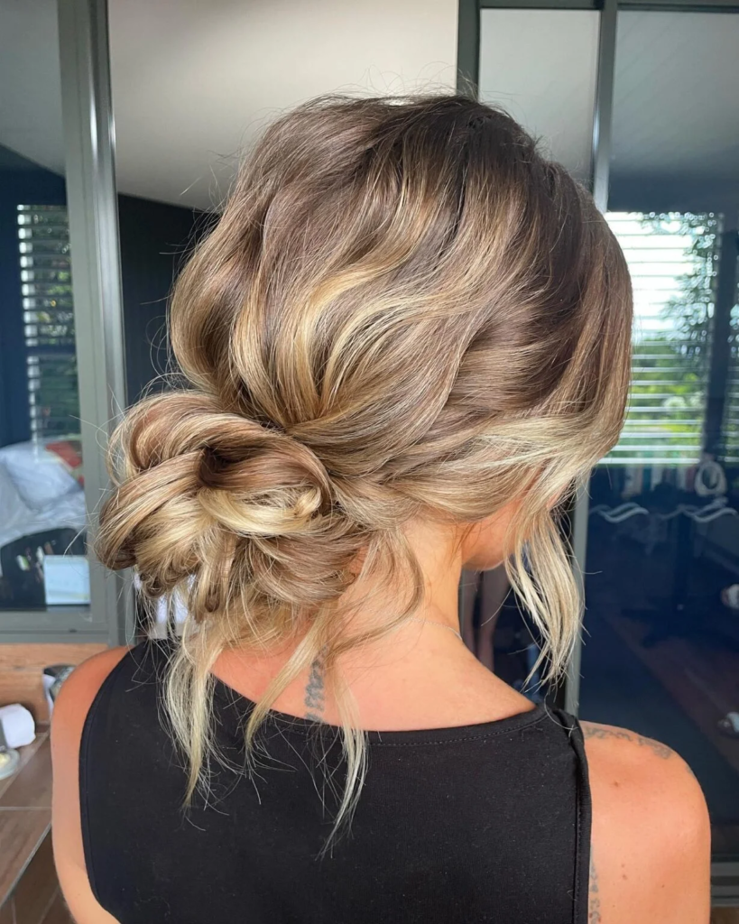 Tousled balayage side bun with sweeping waves and loose face-framing pieces