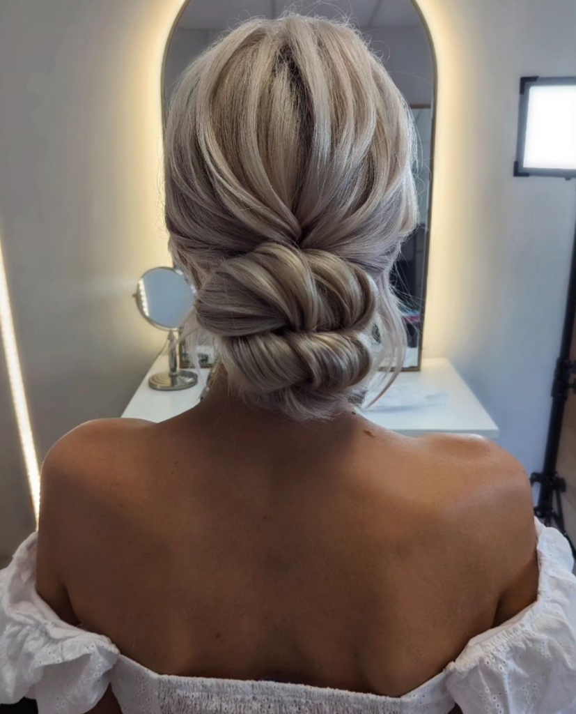 Centered blonde folded low bun with symmetrical loops and a smooth bridal finish