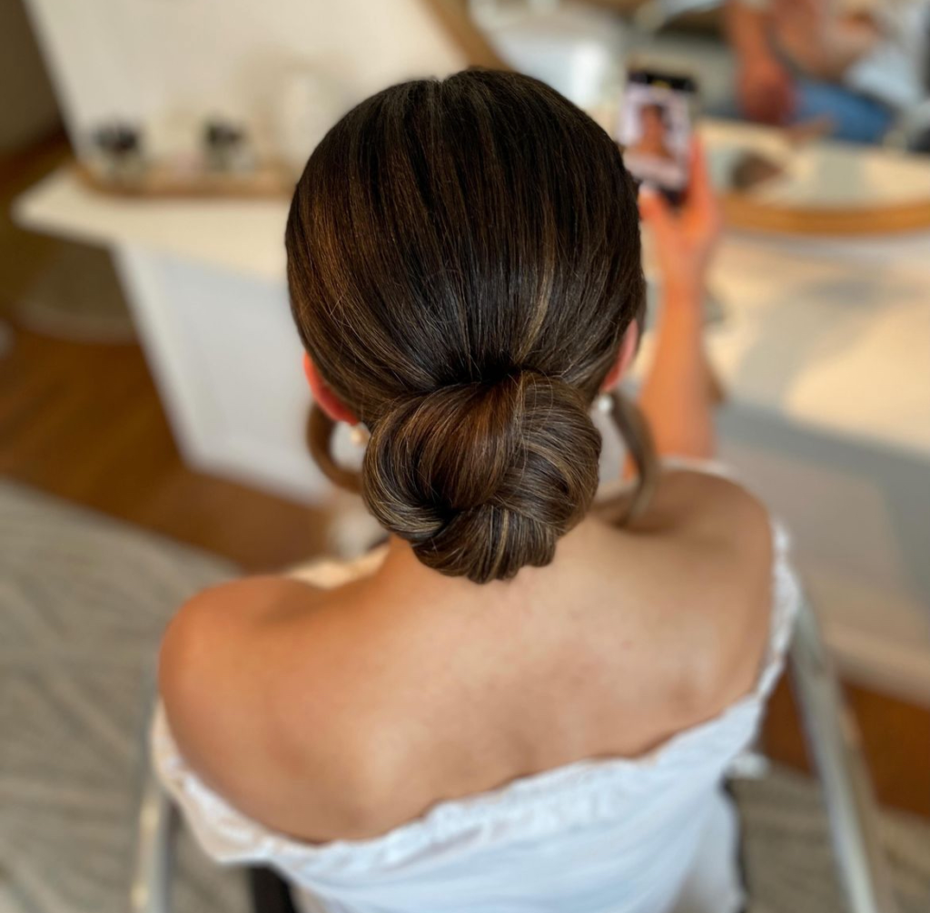 Sleek petite brunette knotted bun centered at the nape with a smooth finish