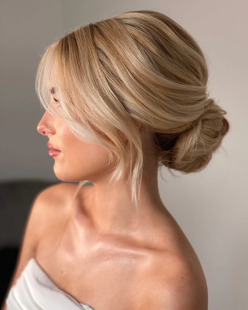 Blonde low bun with curtain bangs and smooth sweeping layers around the face