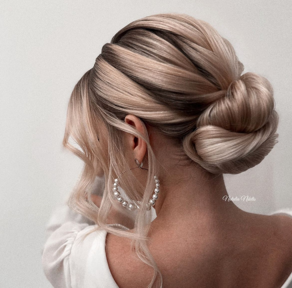 Smooth blonde wrapped low bun with wide folded sections and a neat sculpted finish