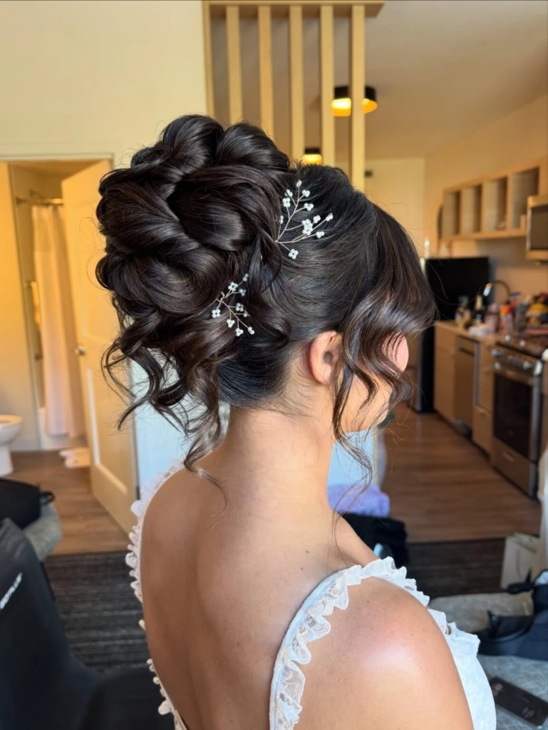 Glossy dark high curled bun with white floral sprigs and face-framing curls
