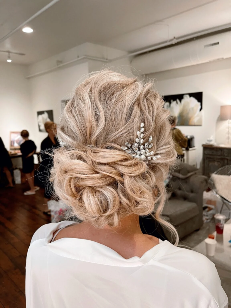 Voluminous blonde low bun with airy loops and a pearl crystal bridal hair comb