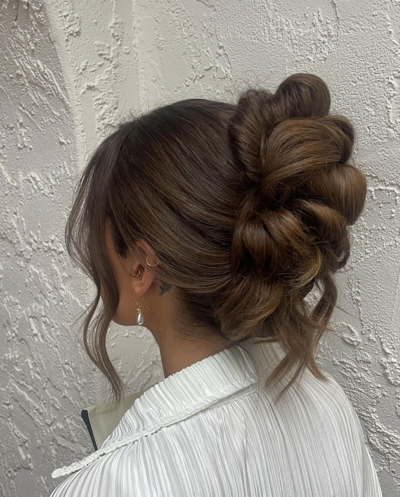 High brunette looped bun with rounded sections and loose curled tendrils