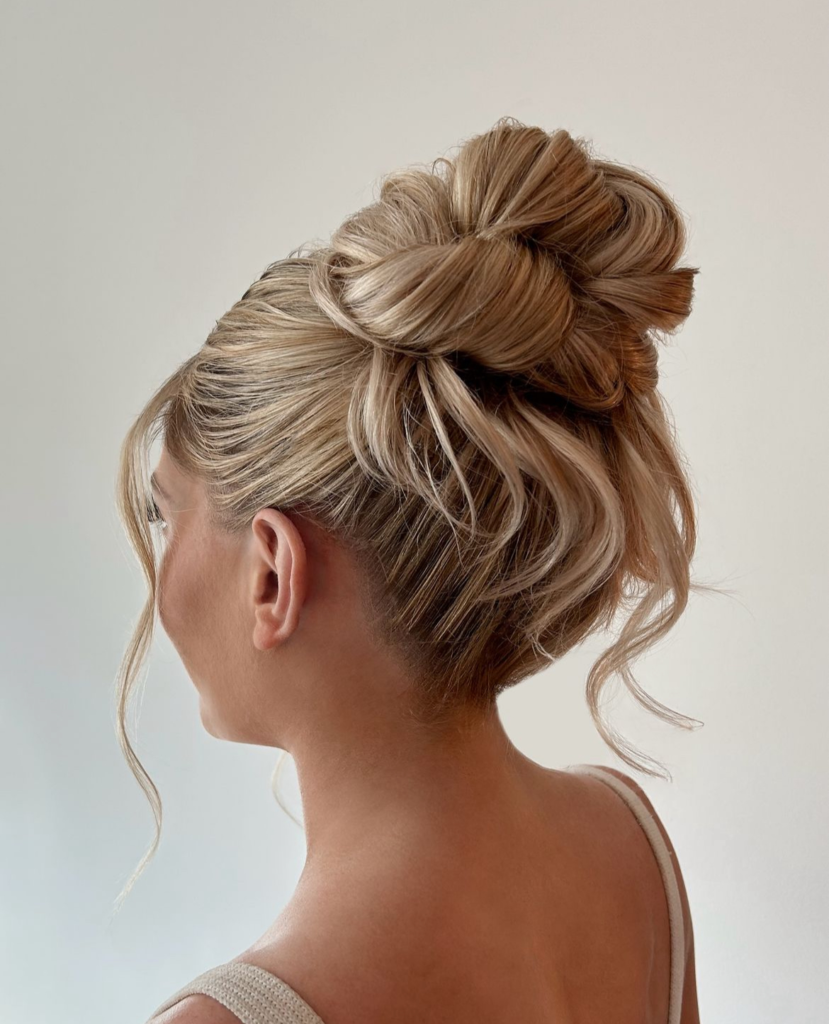 Blonde ribbon-loop high bun with dimensional highlights and loose wispy ends
