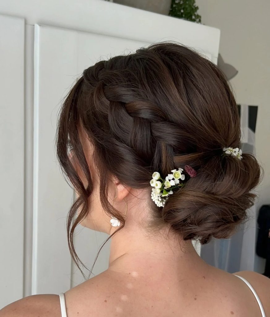 Side-braided brunette low bun decorated with tiny white flowers and curled tendrils