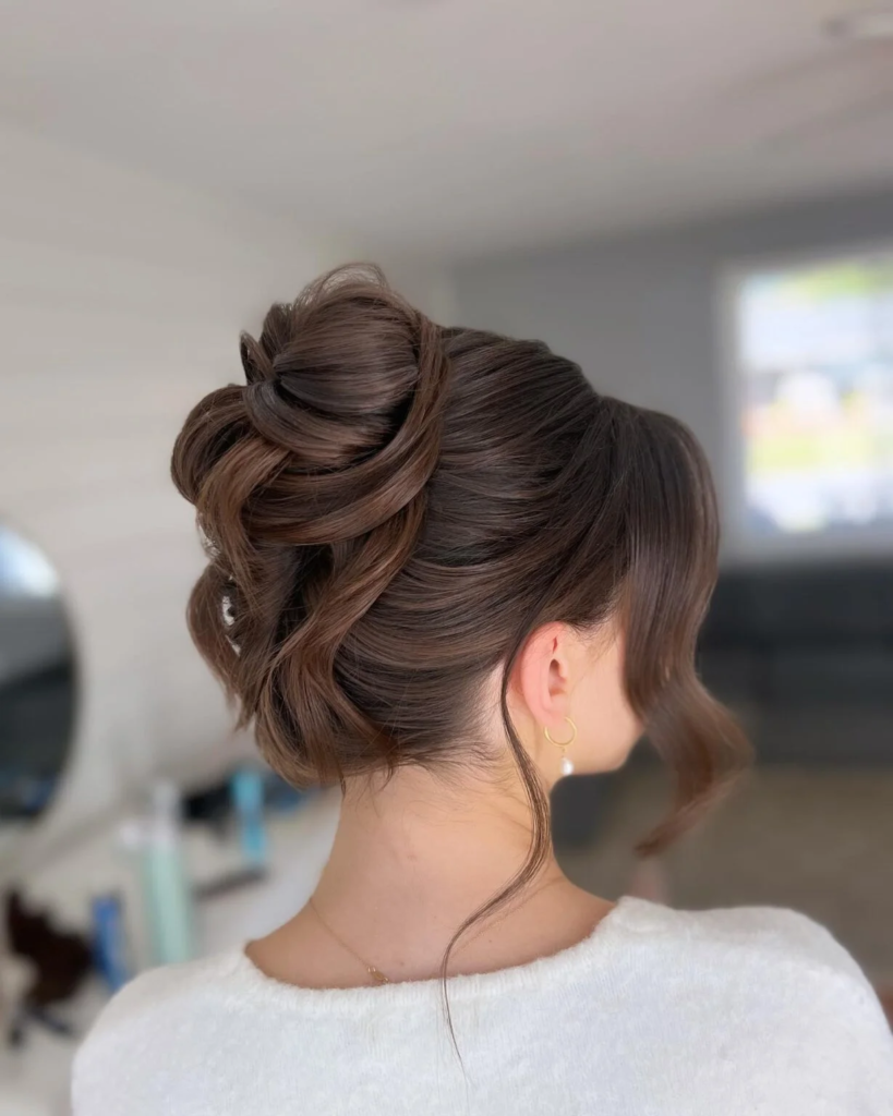 Sculpted brunette high bun with glossy folded sections and side-swept fringe