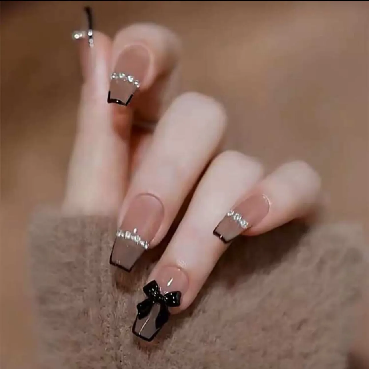 Nude square nails with black outlines crystal borders and a black bow