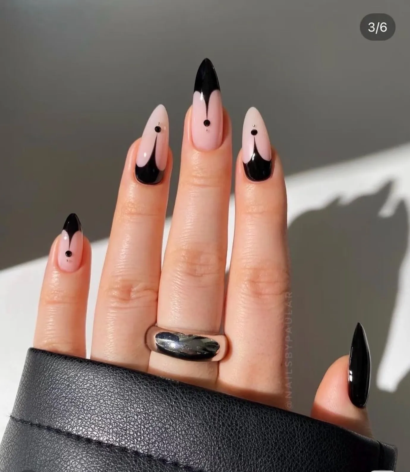 Nude pointed nails with curved black edges and small drop details