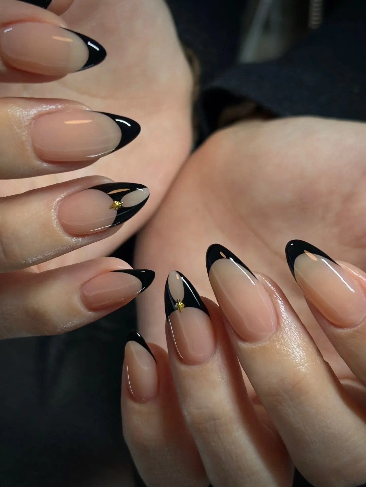 Nude almond nails with black French tips and small gold star accents