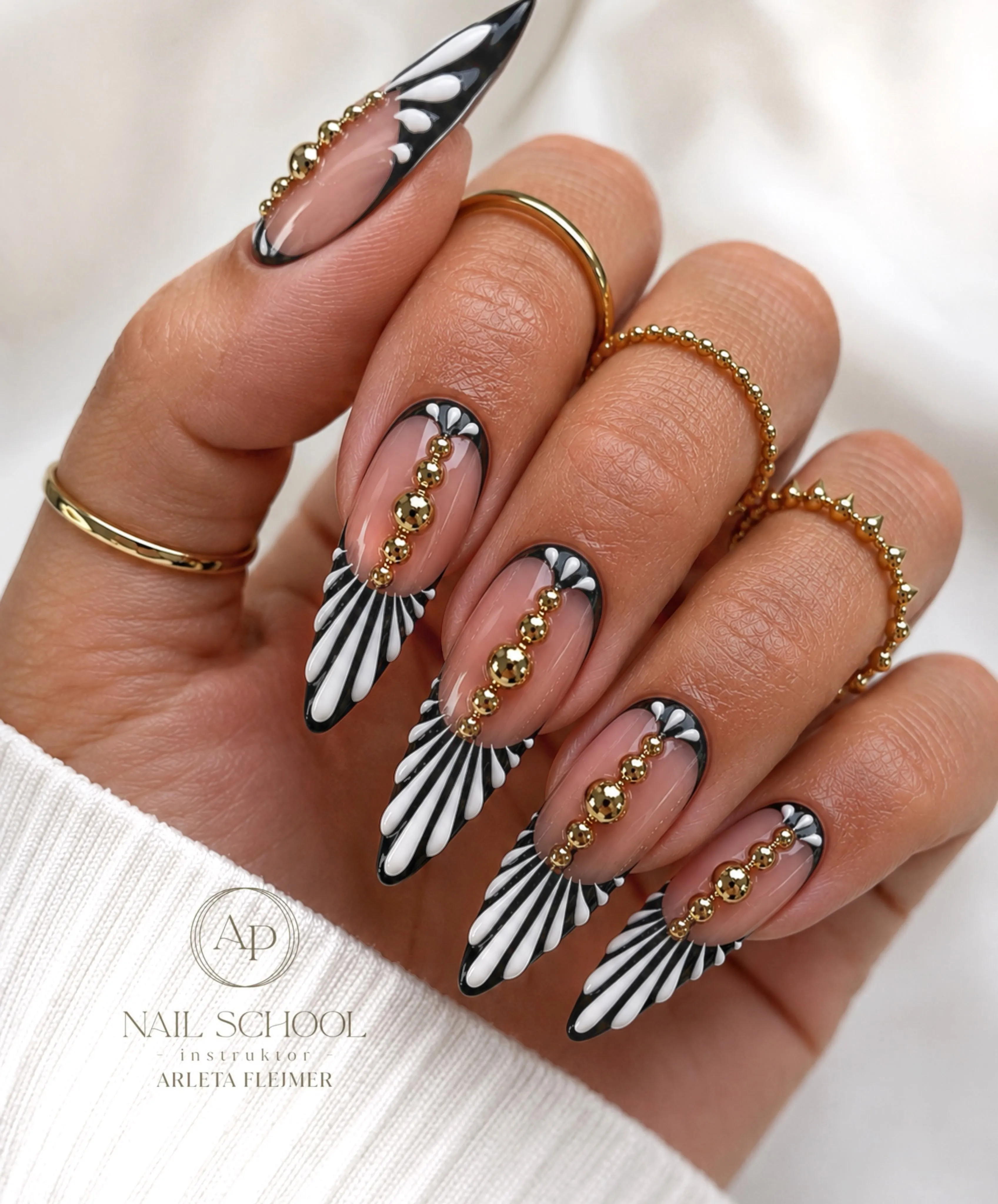 Black and white patterned almond tips with nude centers and gold beads