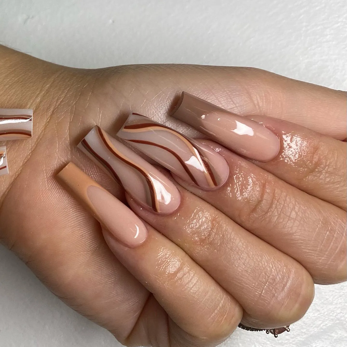 Long square nude nails with brown French tips and flowing brown accent lines