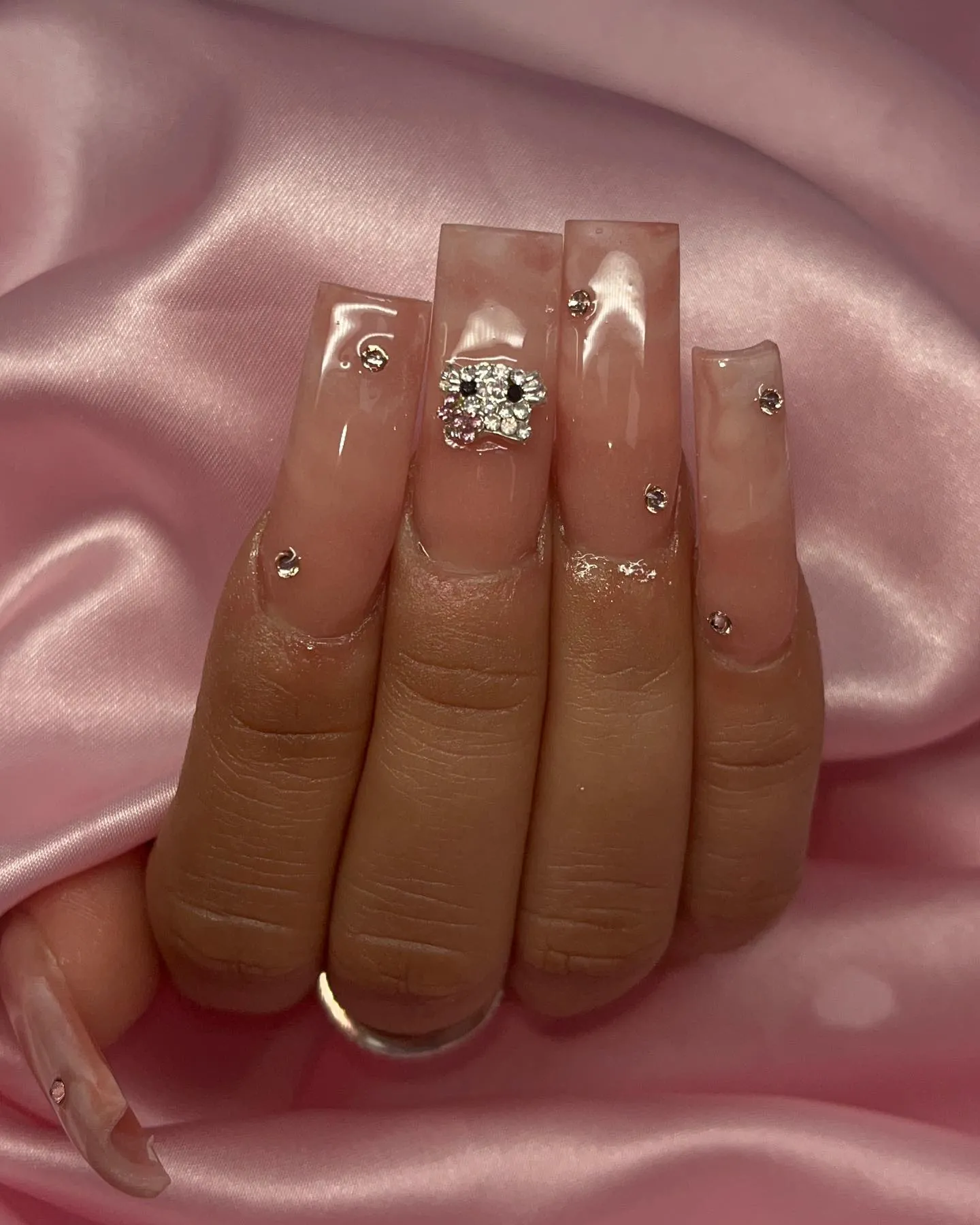 Long nude square nails with small gems and a larger decorative gem charm