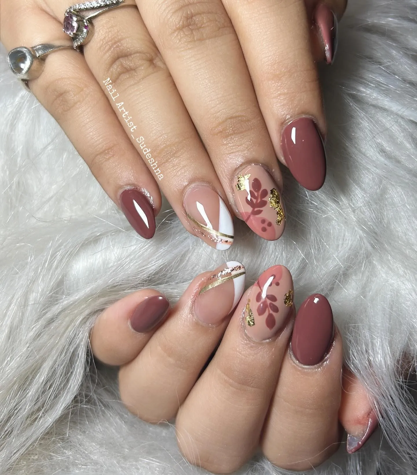Muted reddish brown almond nails with nude leaf accents, white curves and gold flecks