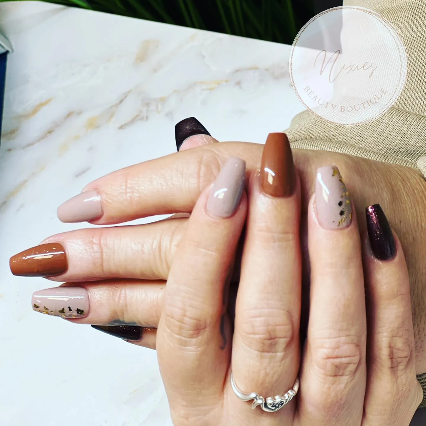 Square nails combining nude, warm brown, dark tips and small dotted accents