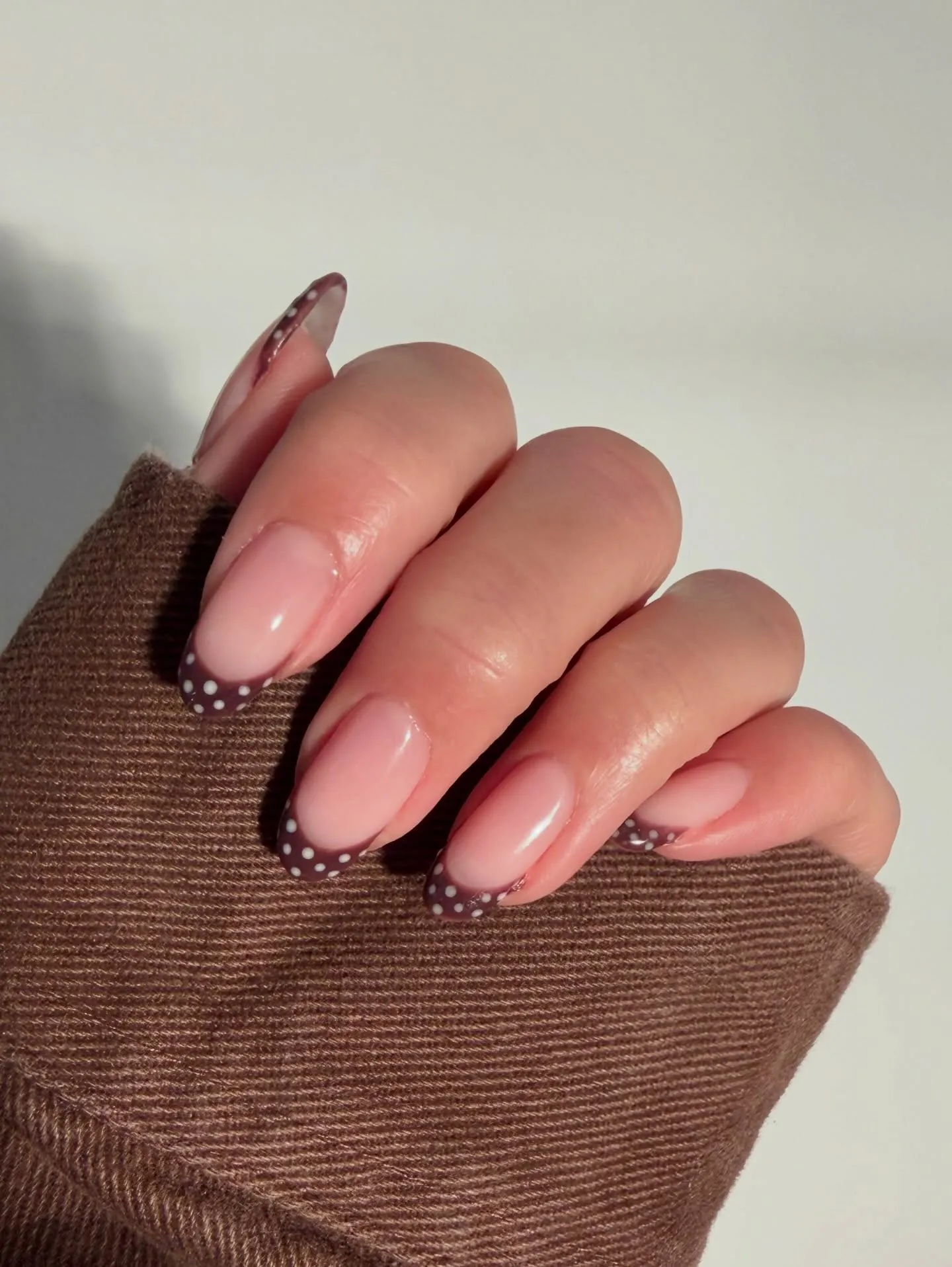 Pink almond nails with narrow dark brown French tips and tiny pale dots