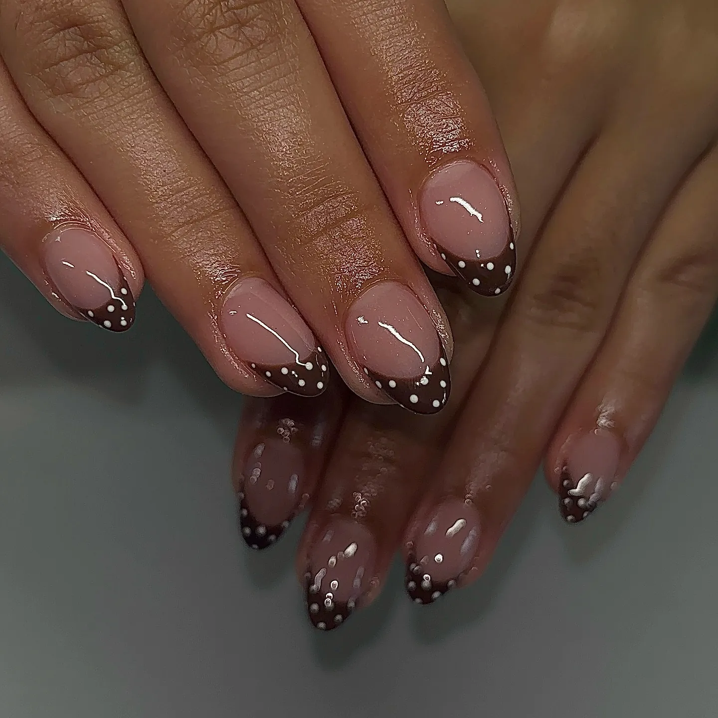 Rounded nude pink nails with brown French tips and white polka dots