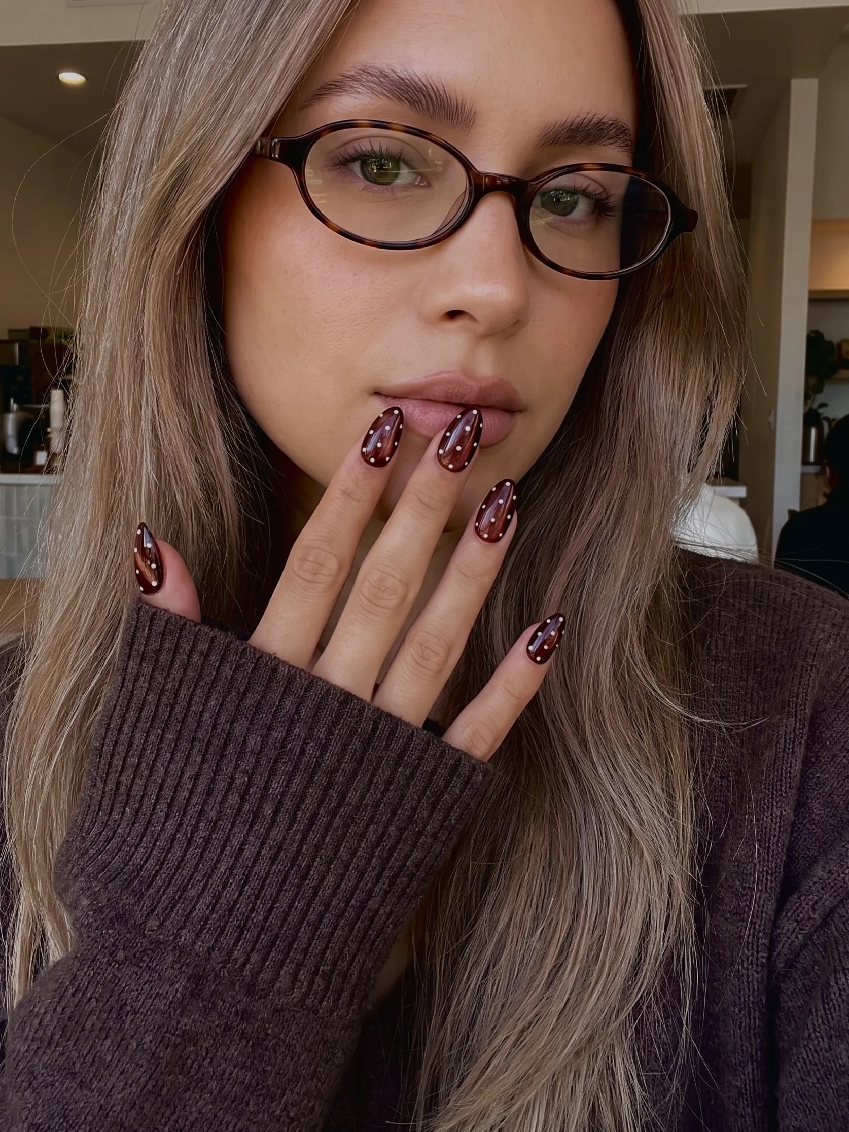 Glossy deep reddish brown almond nails with pale polka dots