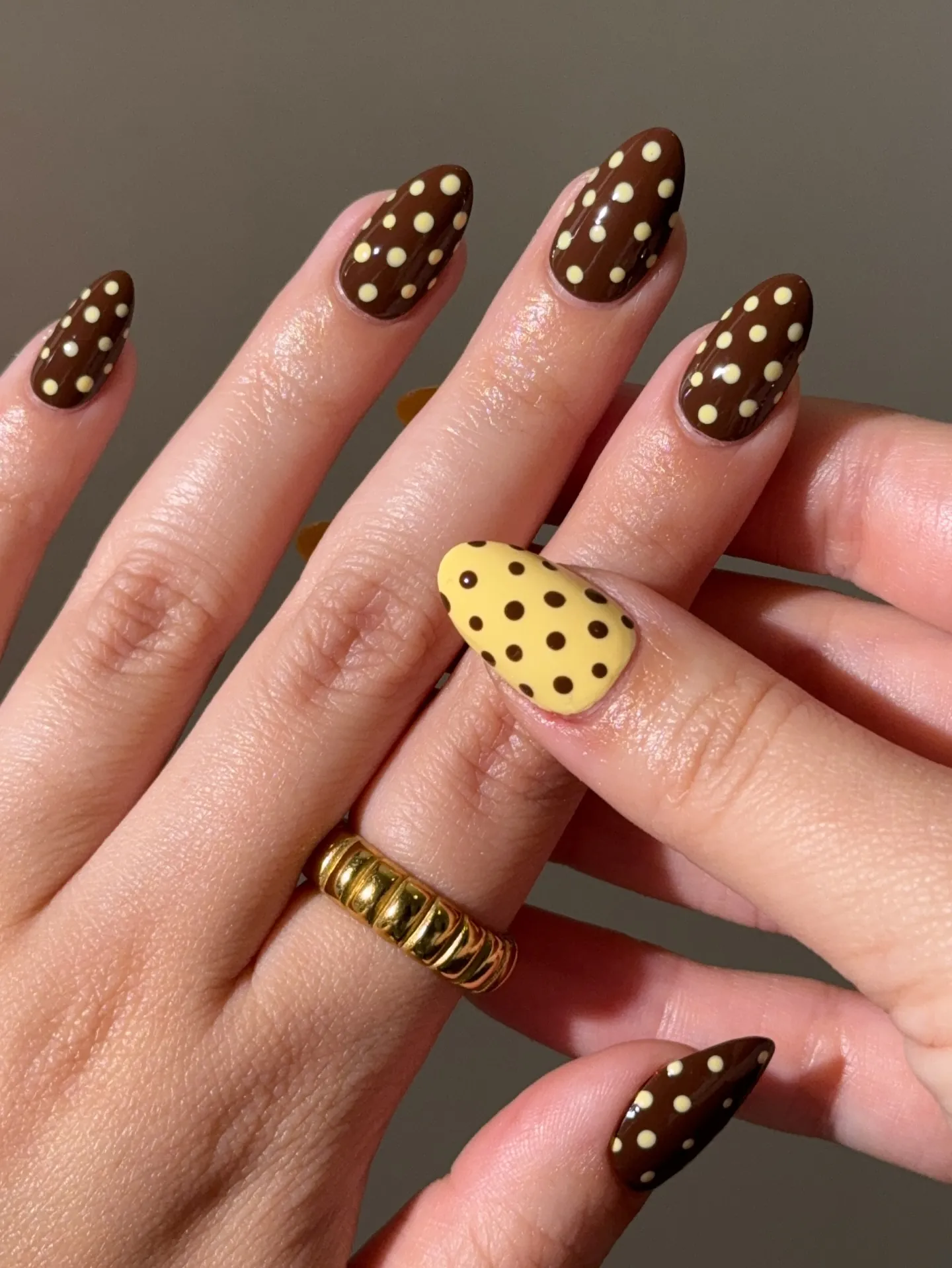 Brown almond nails with pale yellow dots and a yellow accent with brown dots