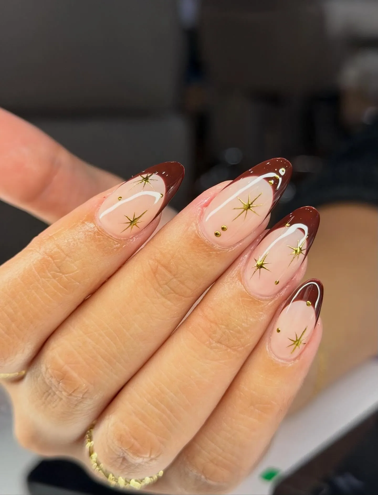 Almond nude nails with pointed brown French tips and fine gold starbursts