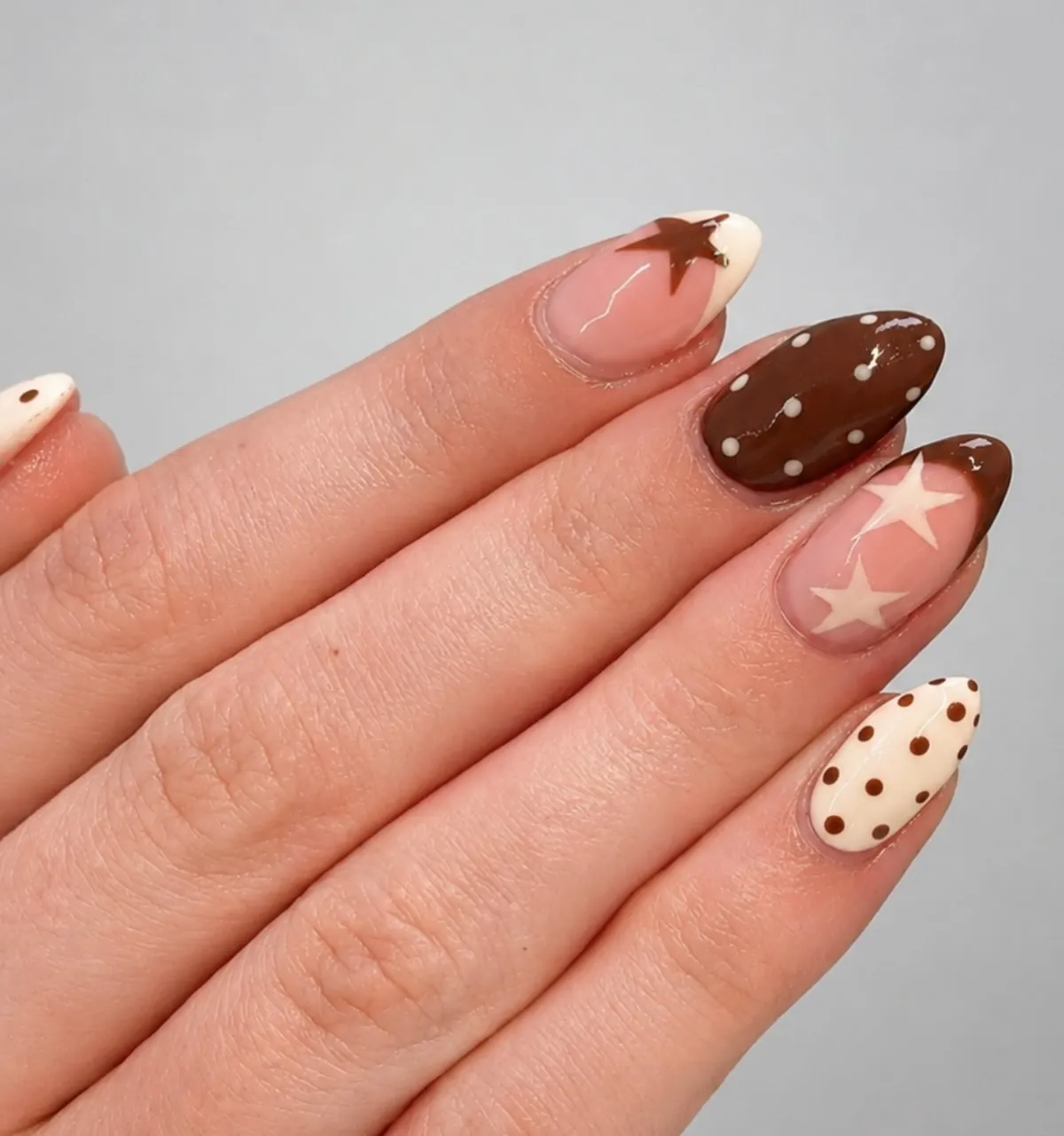 Brown and pink almond nails with white polka dots and large star shapes