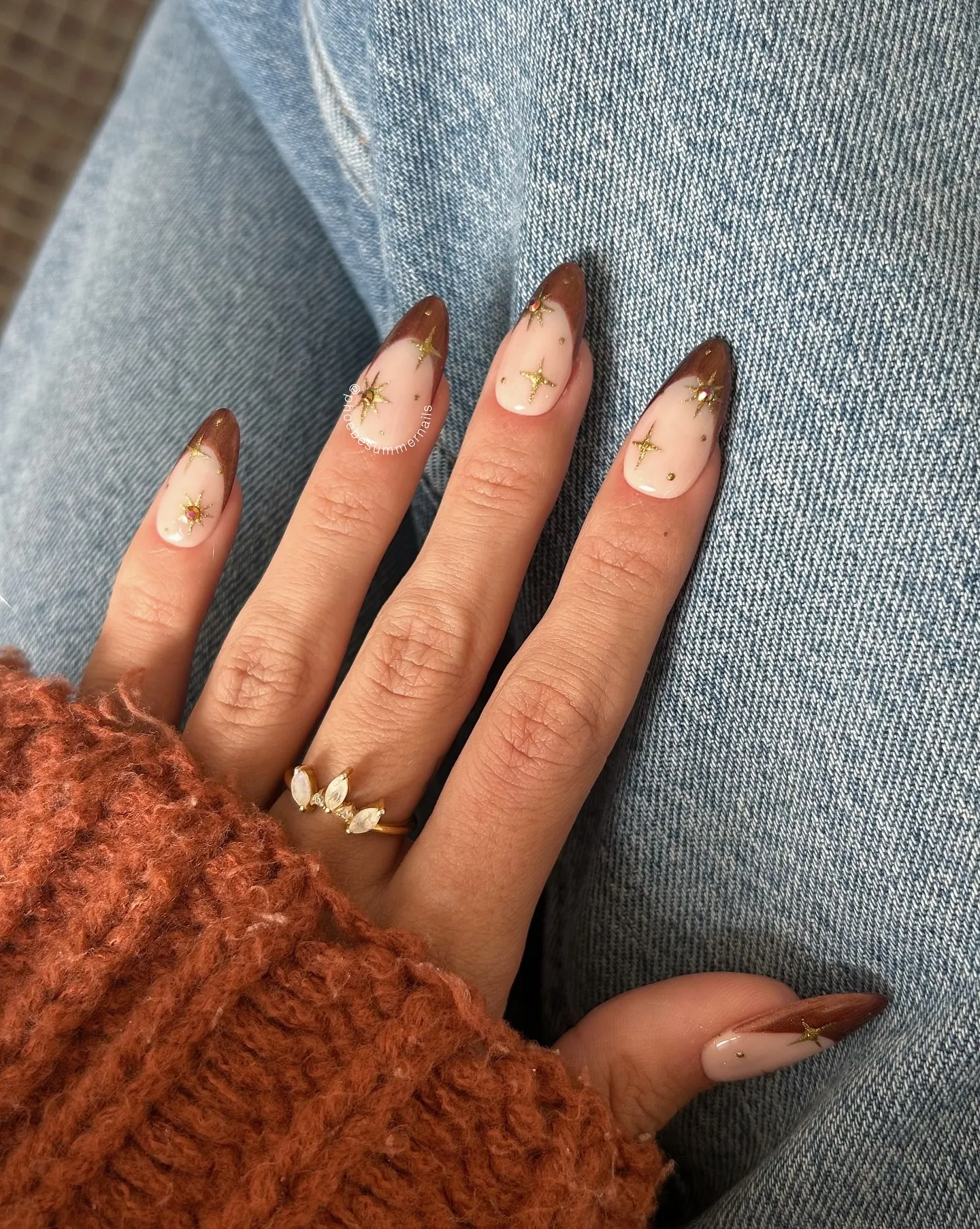 Almond nails with sheer nude polish, thin brown tips and tiny gold stars