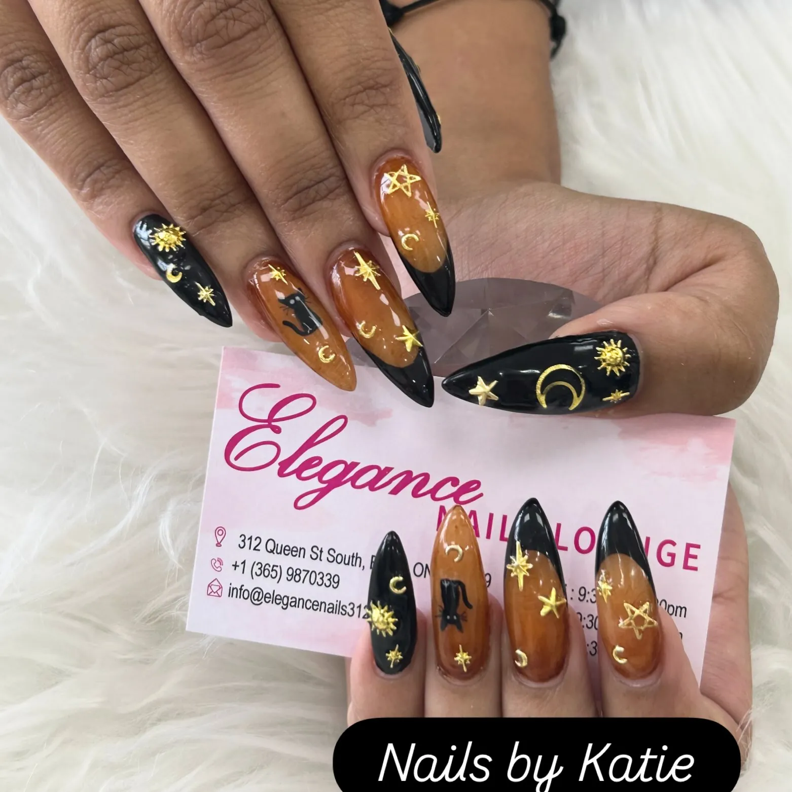 Long dark brown and black nails with gold moons, suns and stars