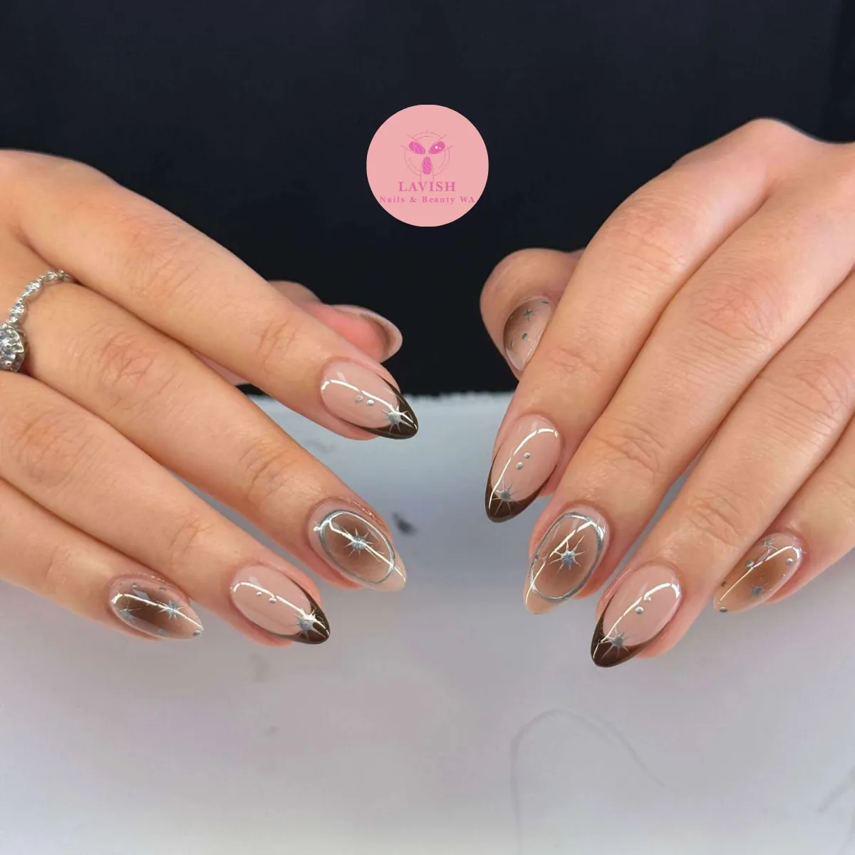 Sheer taupe almond nails with slim brown tips, silver lines and tiny stars