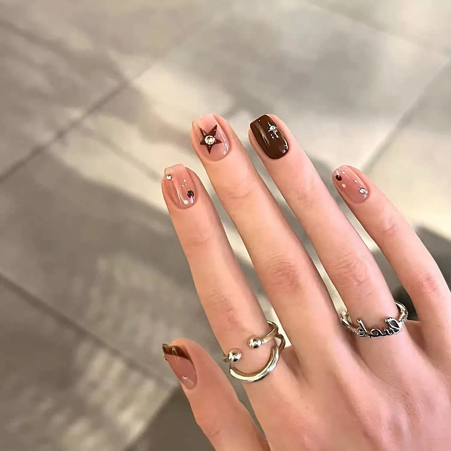 Short blush and chocolate nails with small star accents and rhinestones
