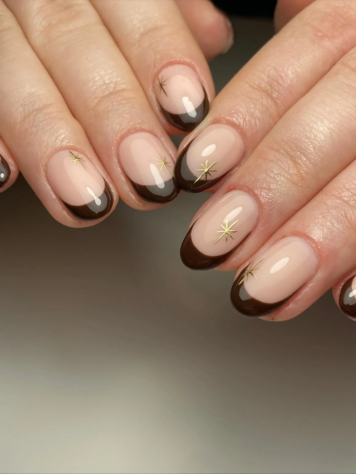 Short rounded nude nails with chocolate French tips and tiny gold stars