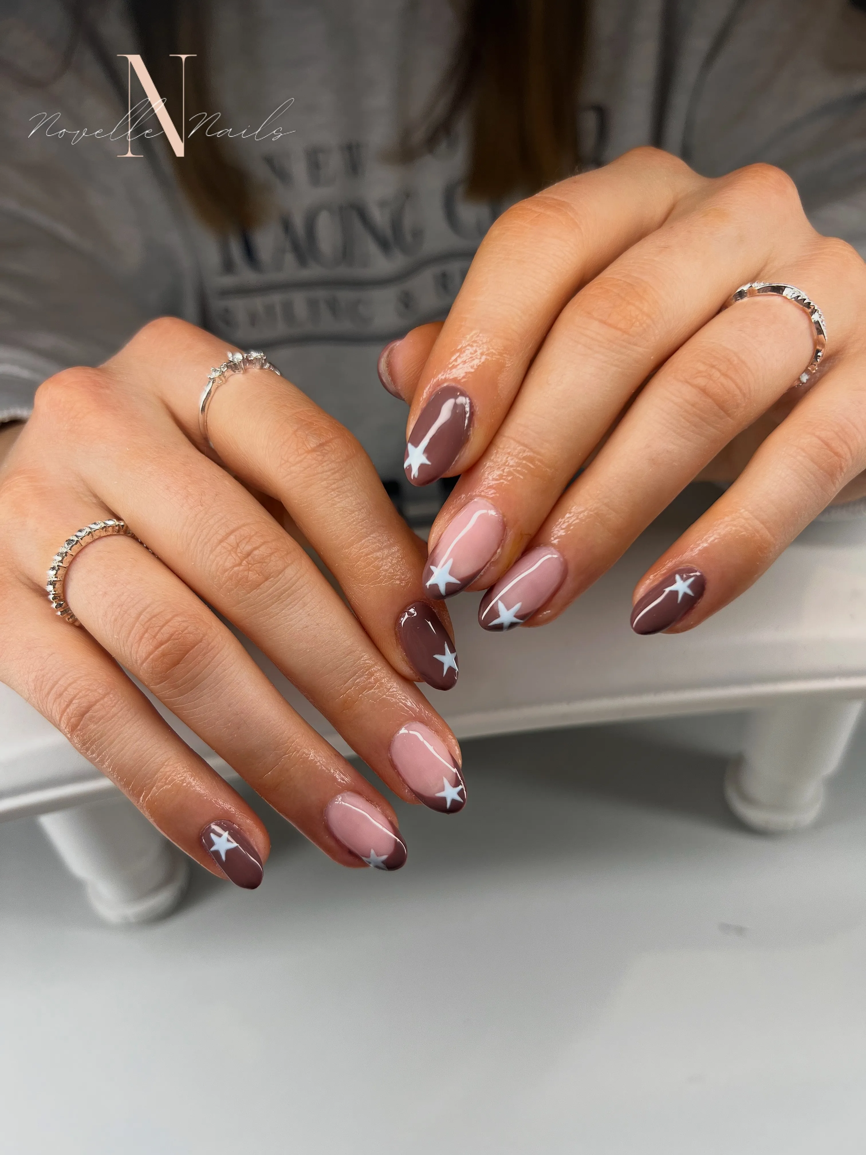 Brown French almond nails with nude sections and white star accents