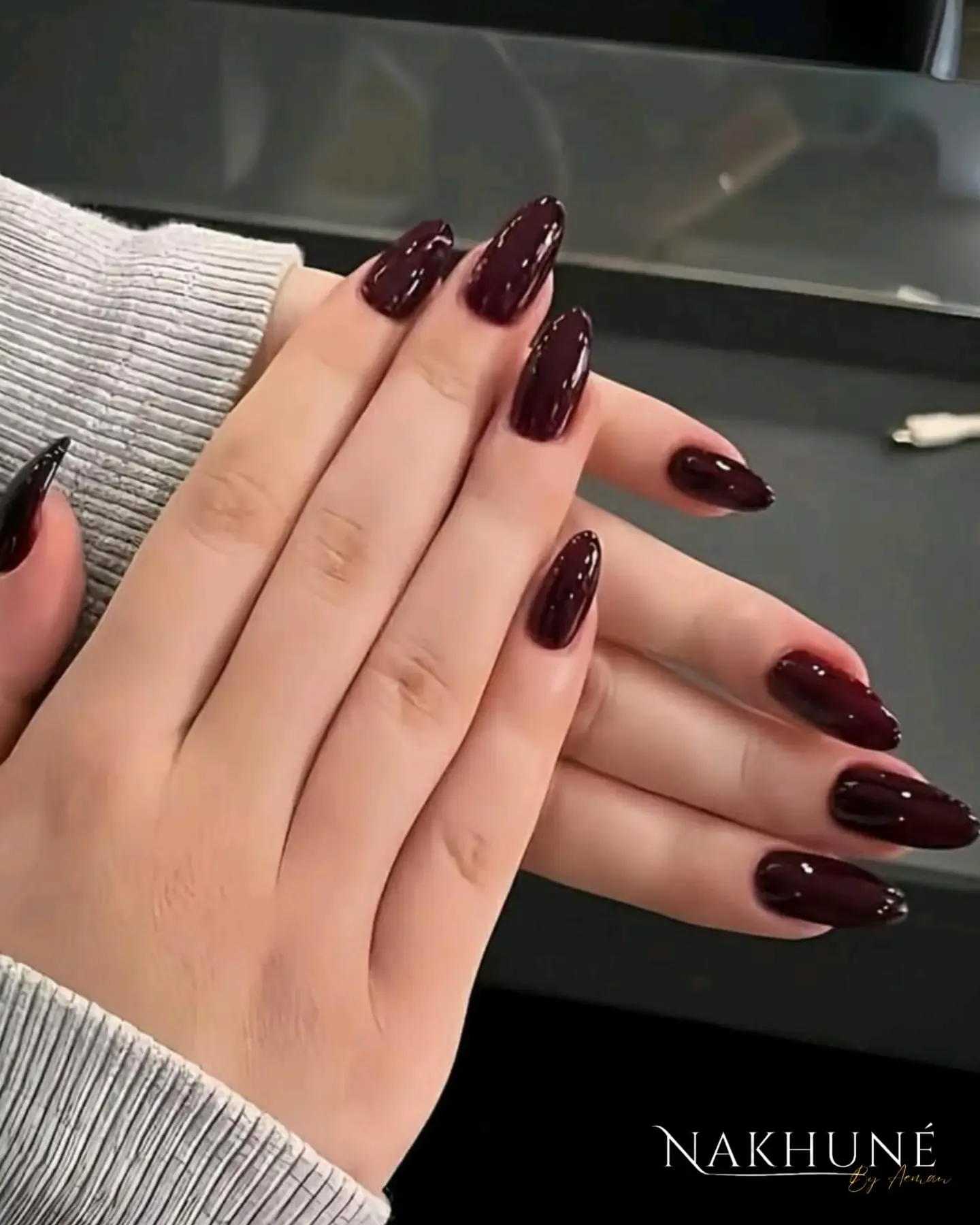 Glossy almond nails in a deep plum burgundy shade