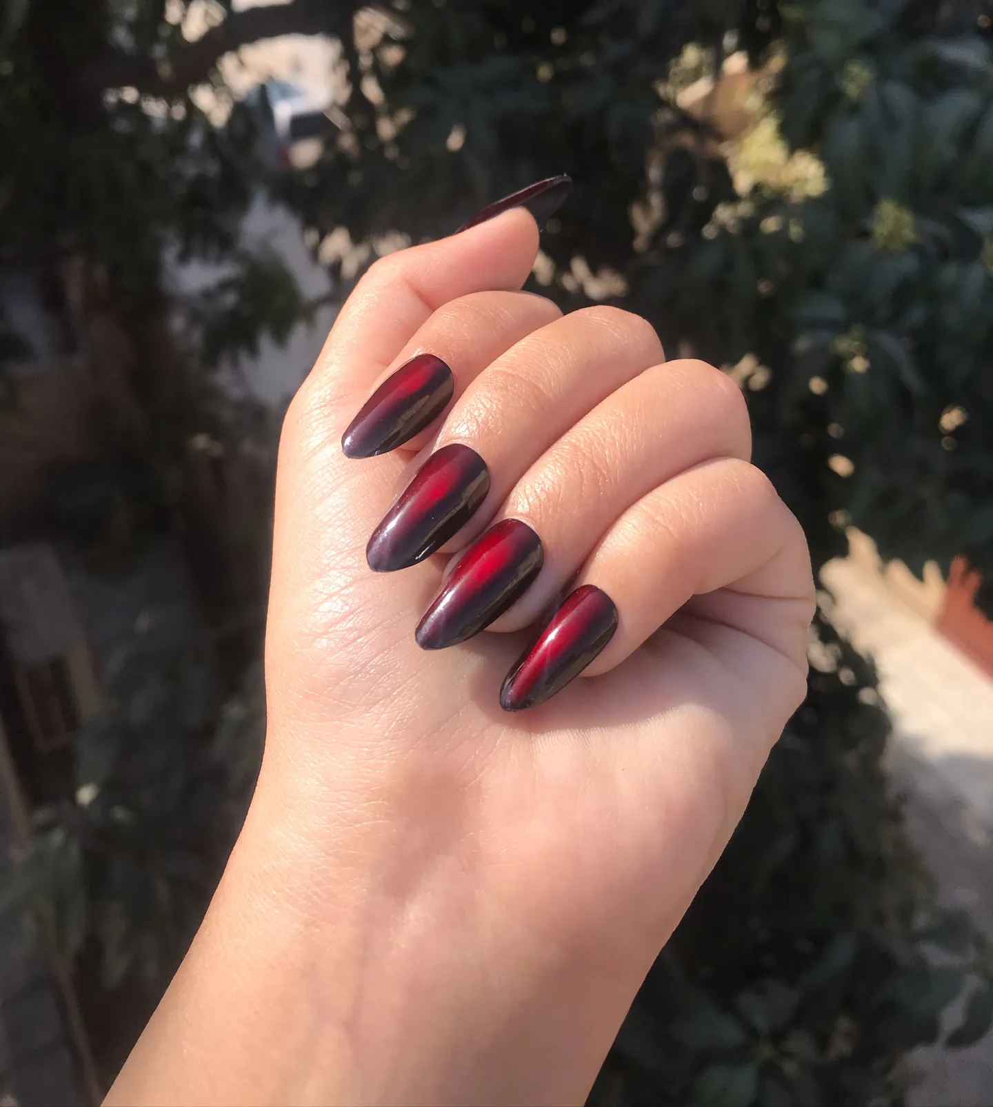 Dark almond nails with luminous red centers and deep burgundy edges
