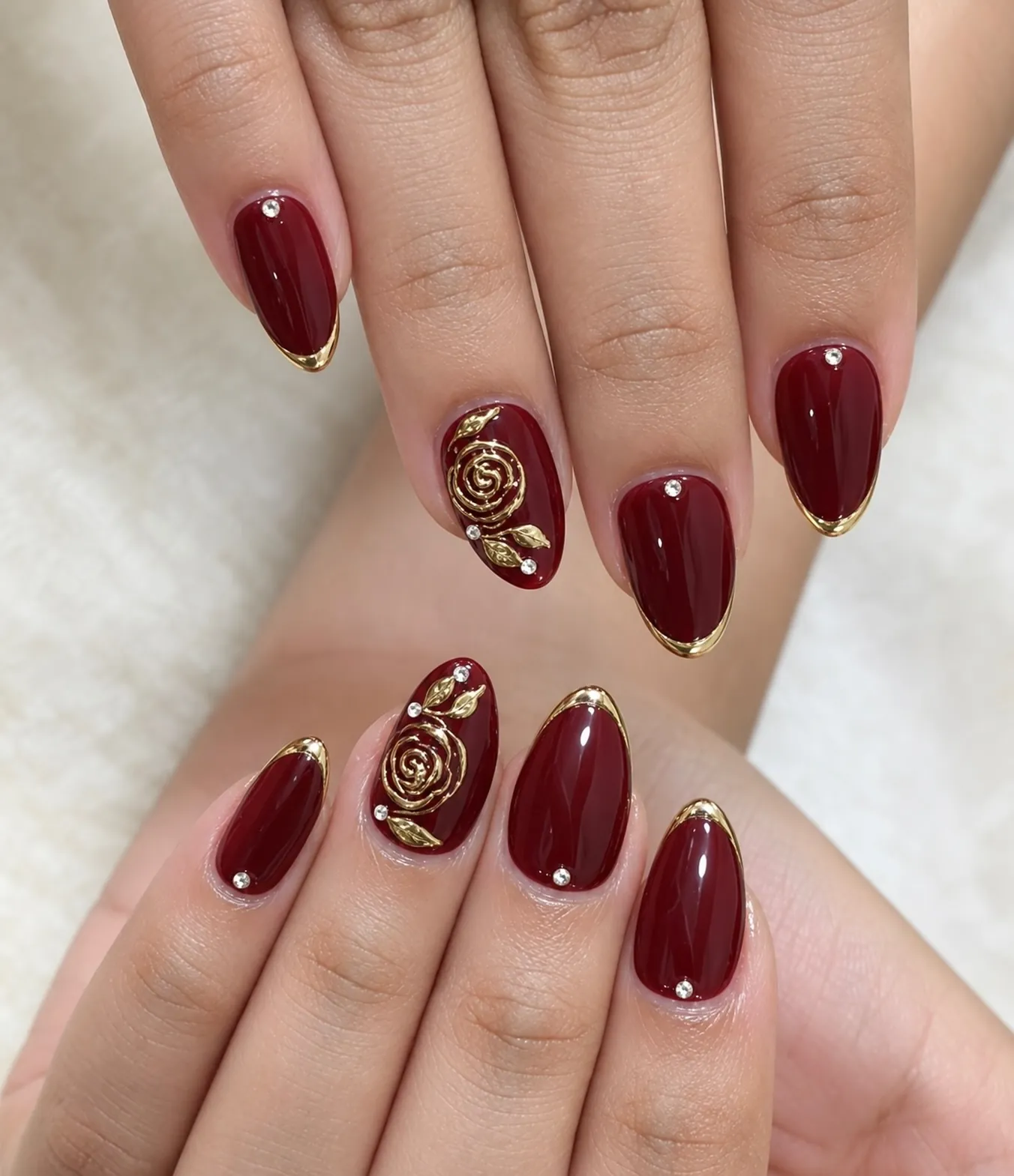 Glossy burgundy almond nails with gold rose artwork and fine borders