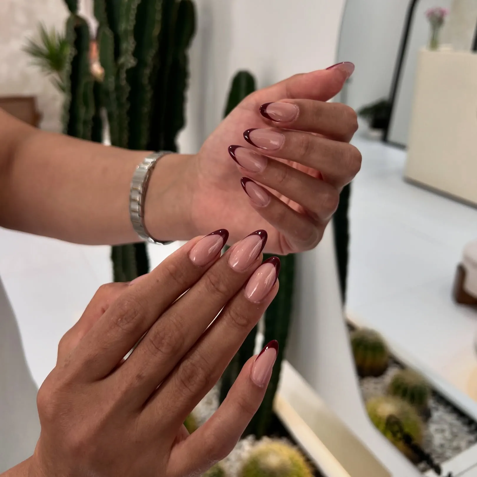 Glossy nude pink almond nails with very dark burgundy edges