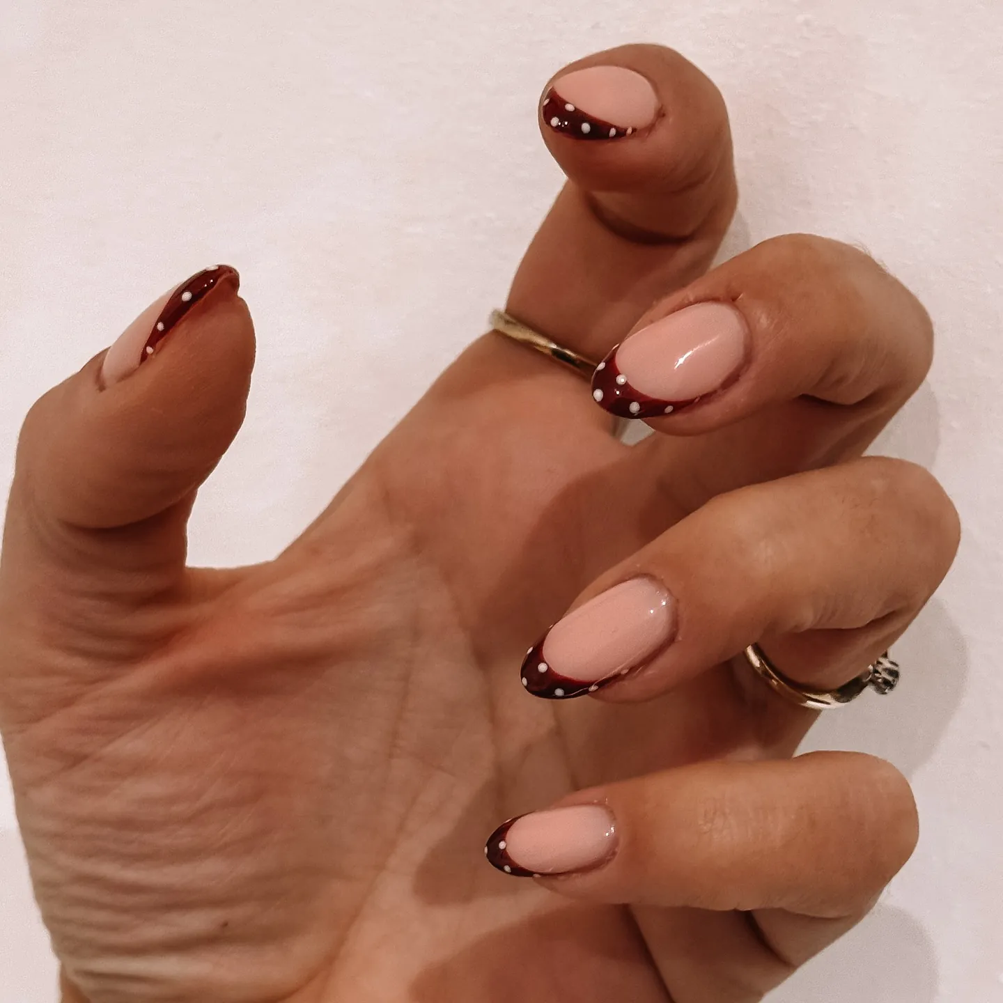 Short rounded pink nails with burgundy tips and small pale dots