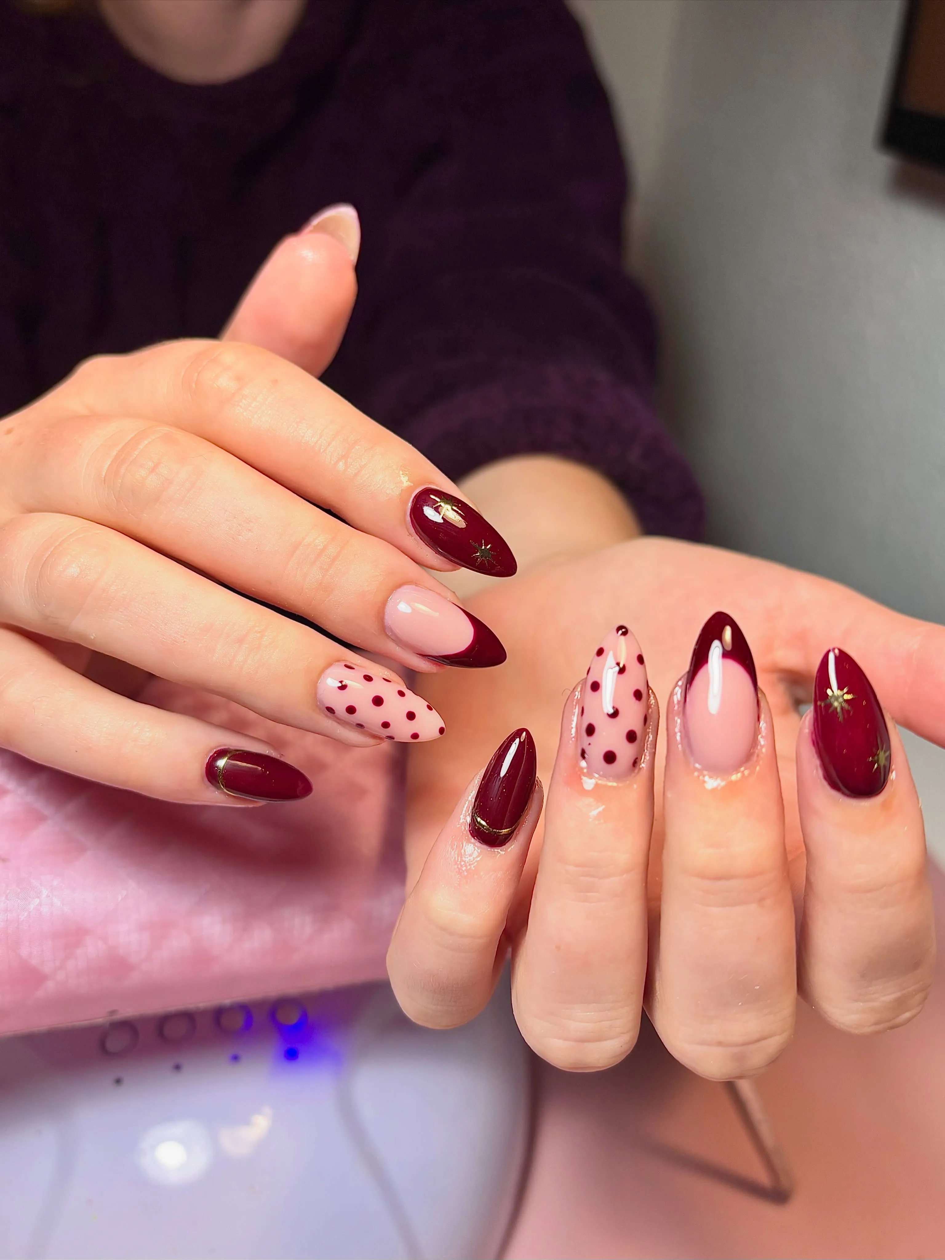 Almond nails with burgundy color, French tips, gold stars and dotted pink accents