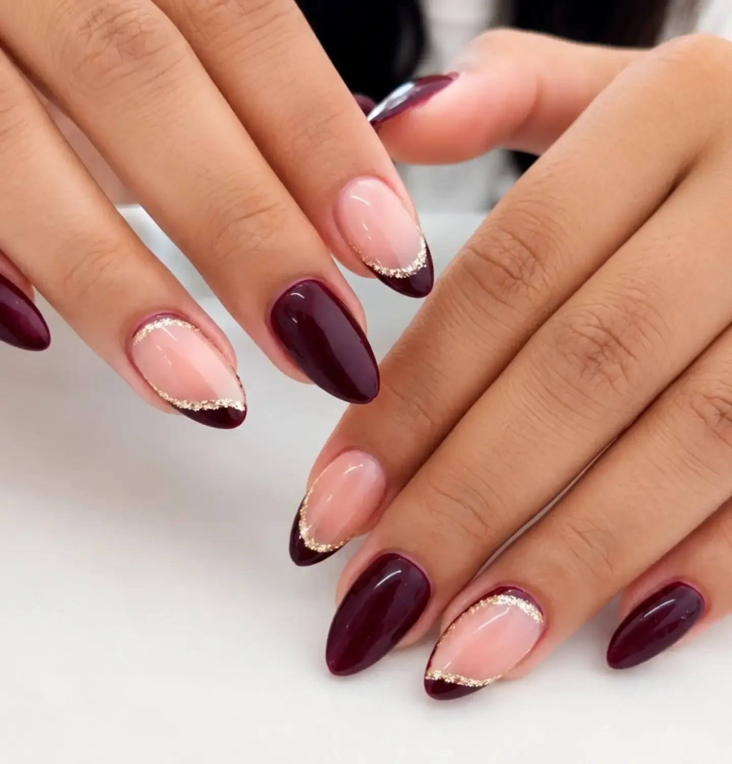 Almond nails mixing solid burgundy with pink French tips edged in gold