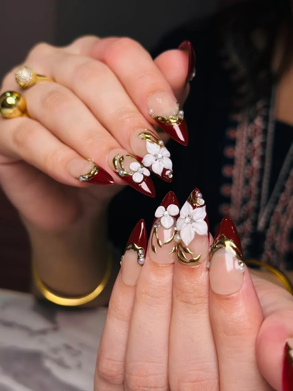 Pointed burgundy French nails with raised white flowers and gold accents