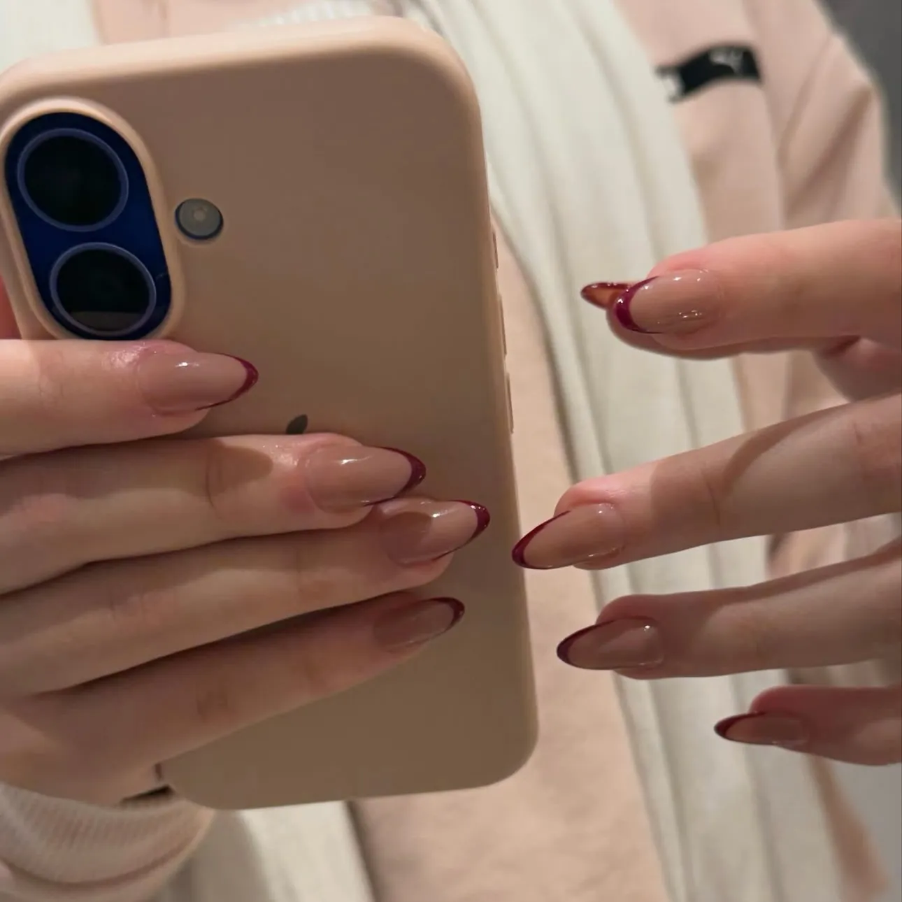 Glossy pink almond nails with slim burgundy French tips