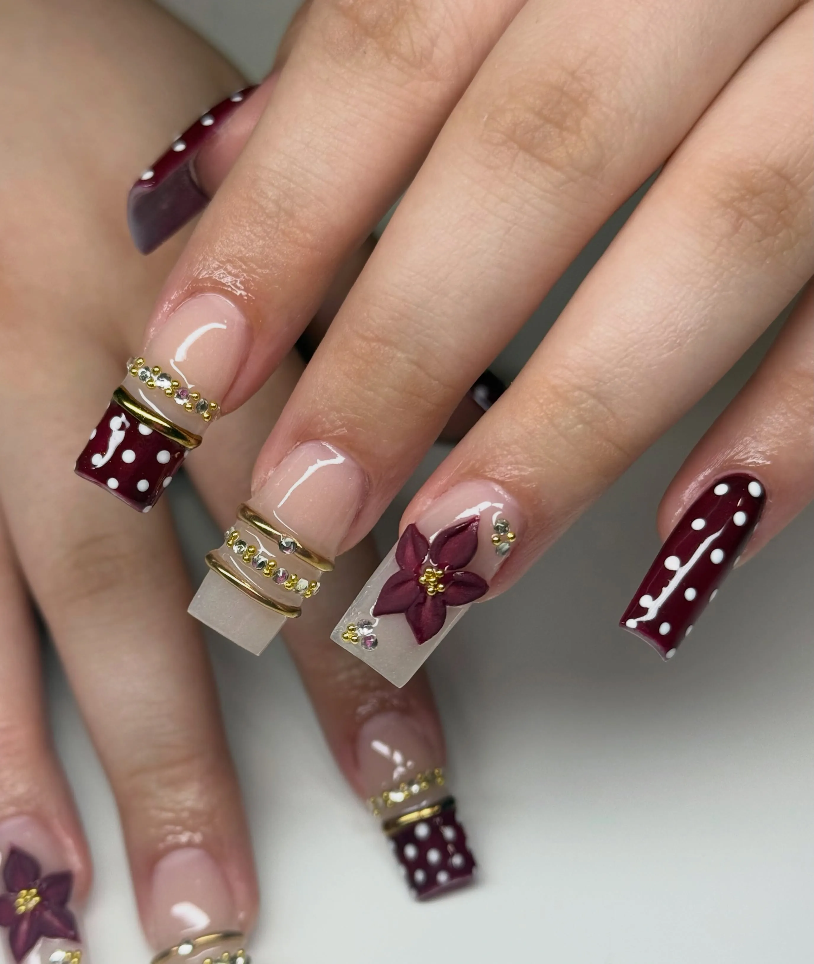 Long square nails with burgundy dots raised flowers gold bands and gems