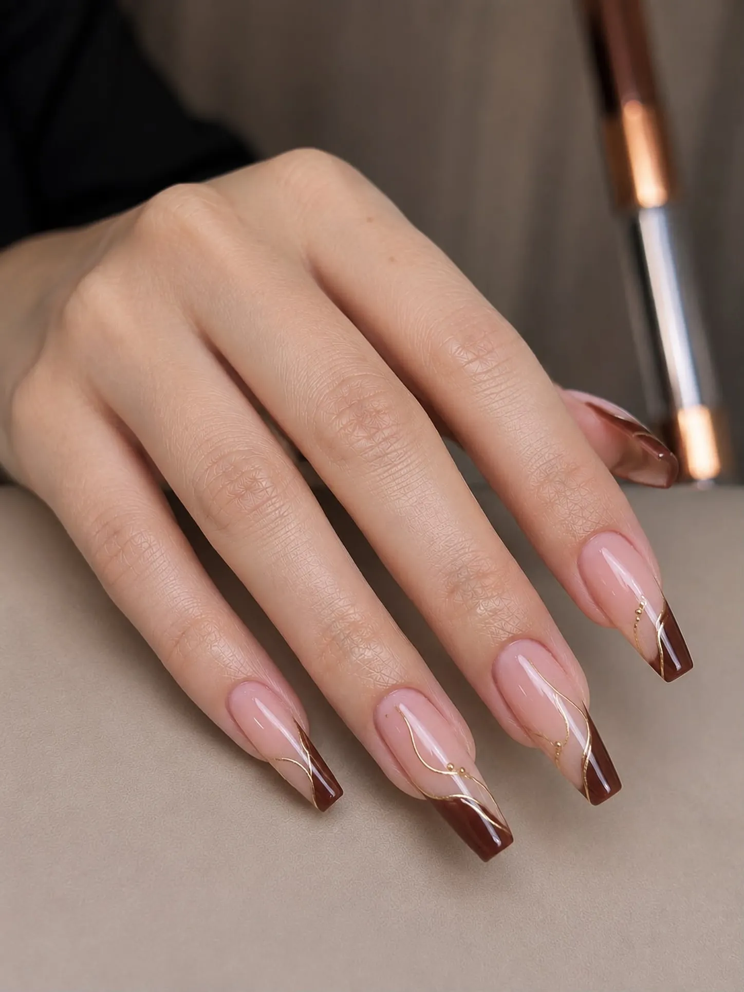 Long square nails with brown diagonal tips and fine gold swirls