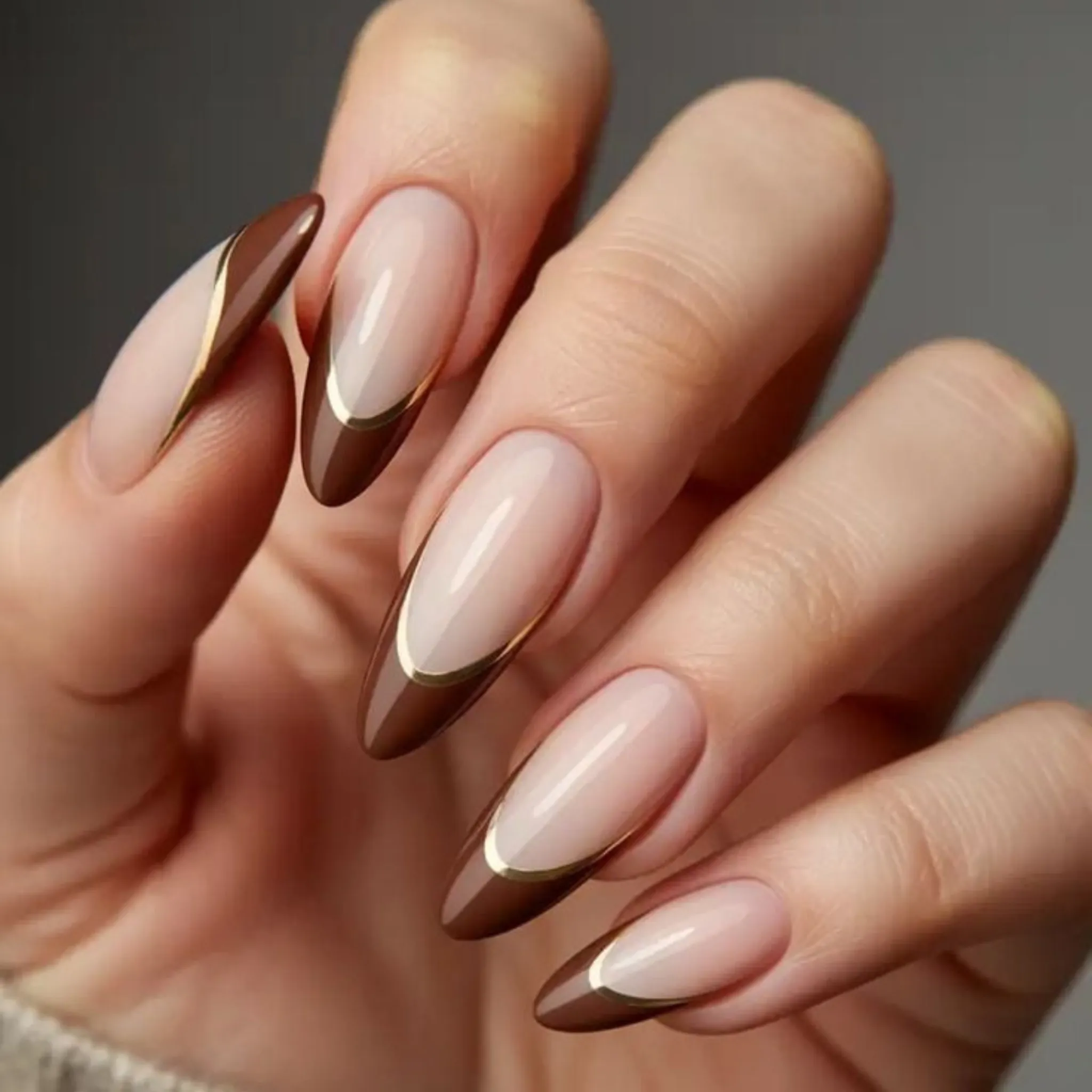 Nude almond nails with brown French tips and fine gold borders