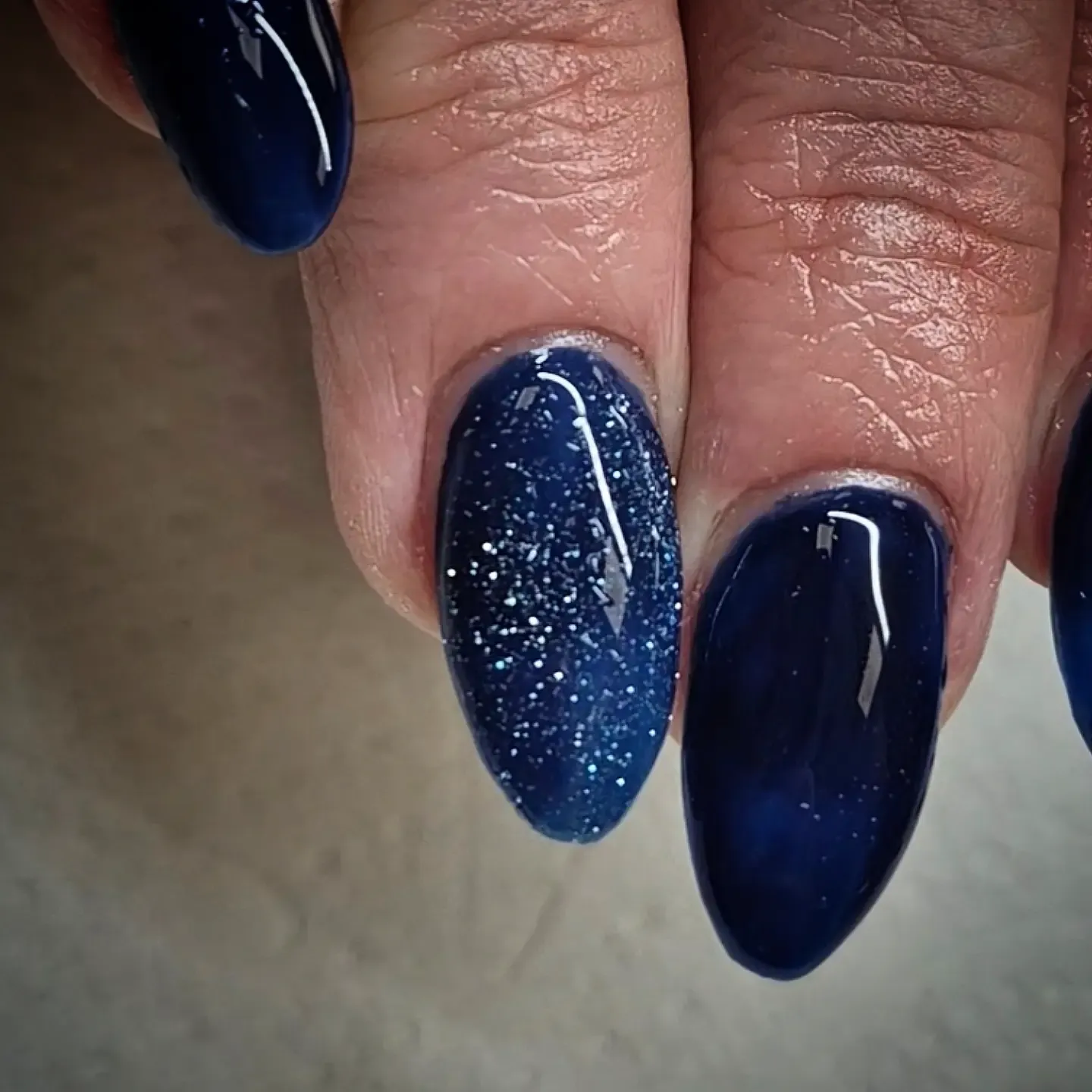 Glossy navy almond nails with one blue glitter accent nail