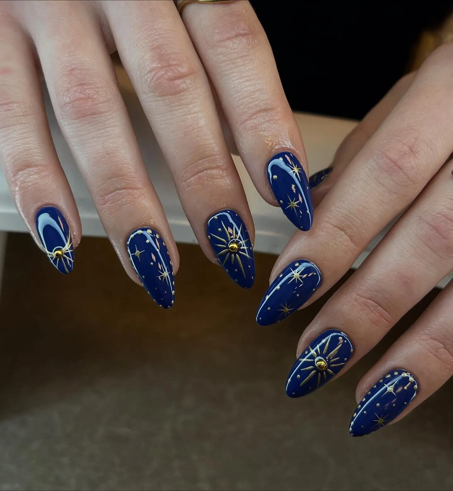 Navy almond nails with gold starbursts and fine pale curved lines