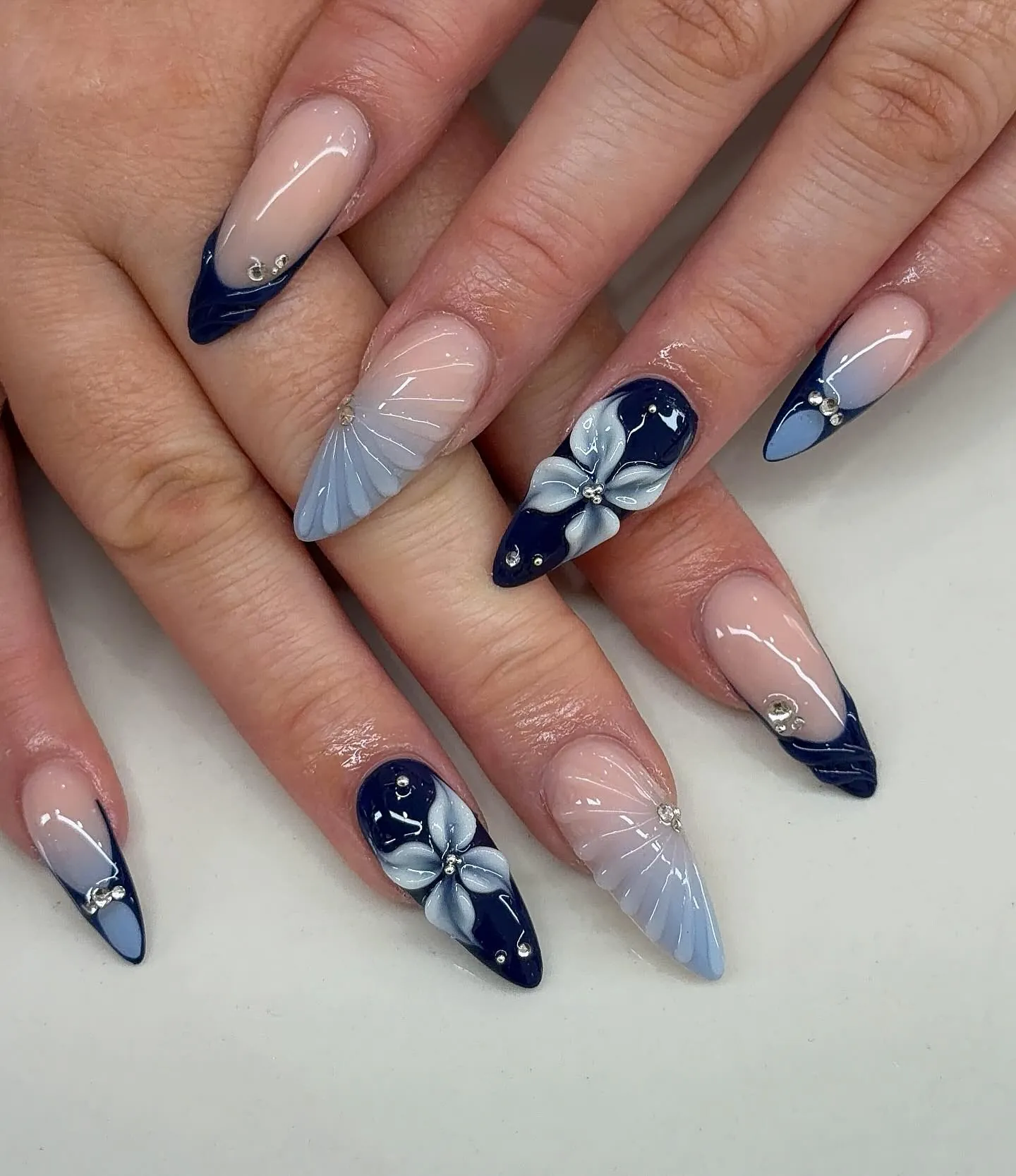 Navy French nails with pale blue flowers, shell-like ridges and small gems